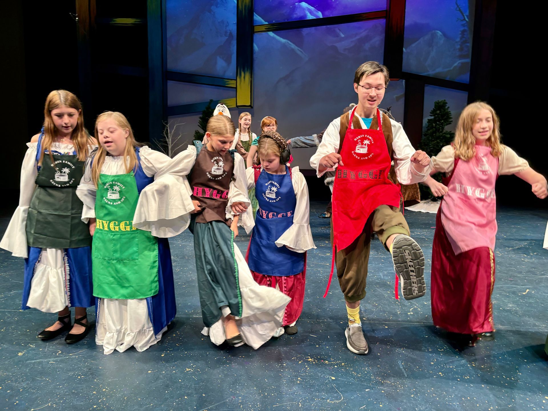 Children in colorful costumes dance on stage.