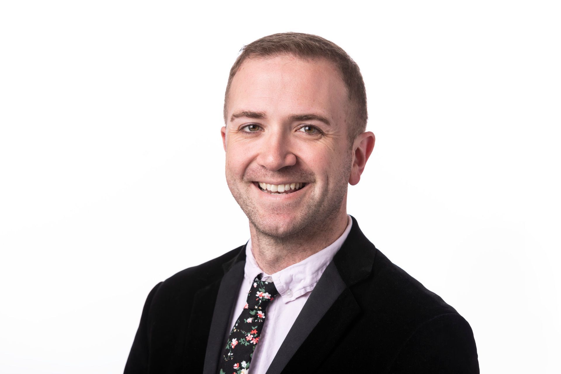 Smiling man in a black suit and patterned tie against a white background