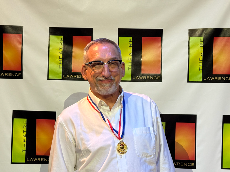 Man wearing a medal stands smiling in front of a Lawrence backdrop
