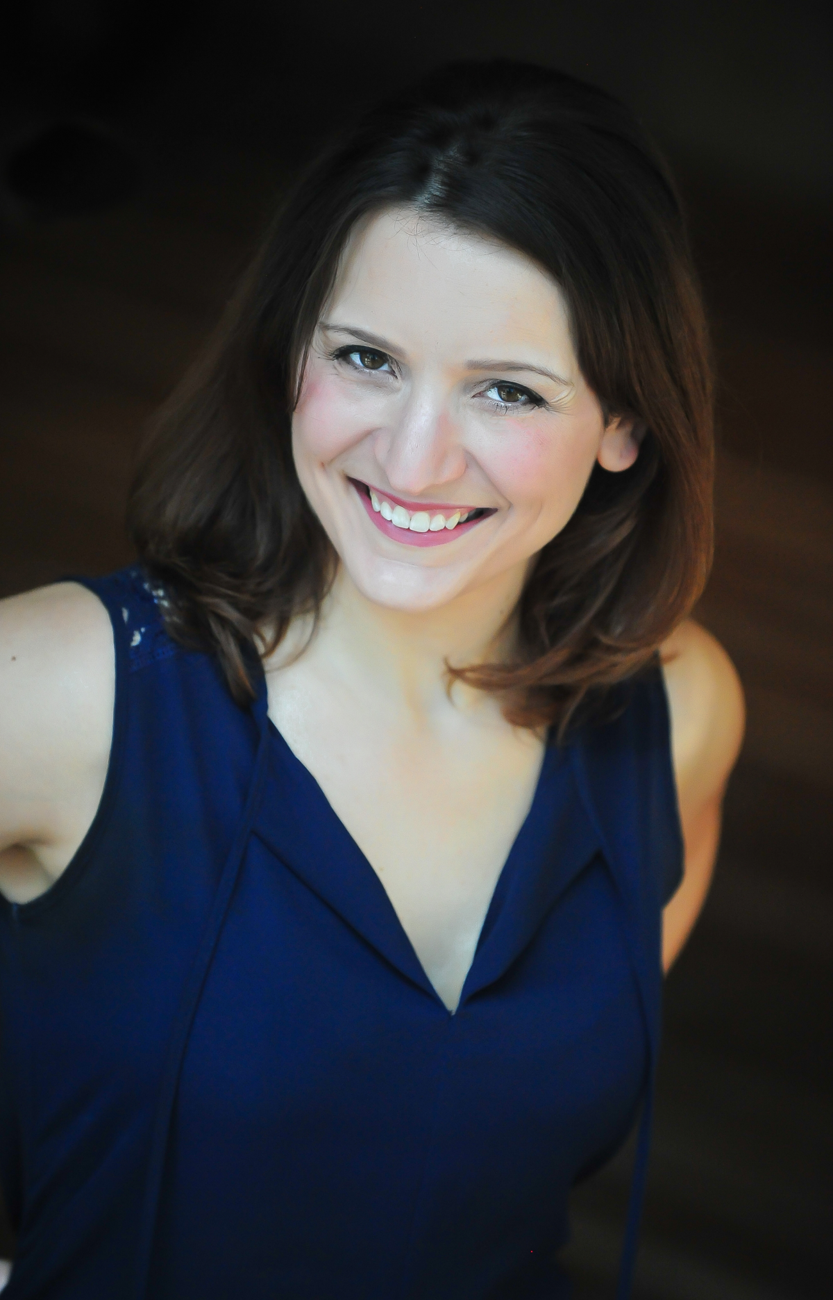 Smiling woman in a dark blue sleeveless top against a dark background