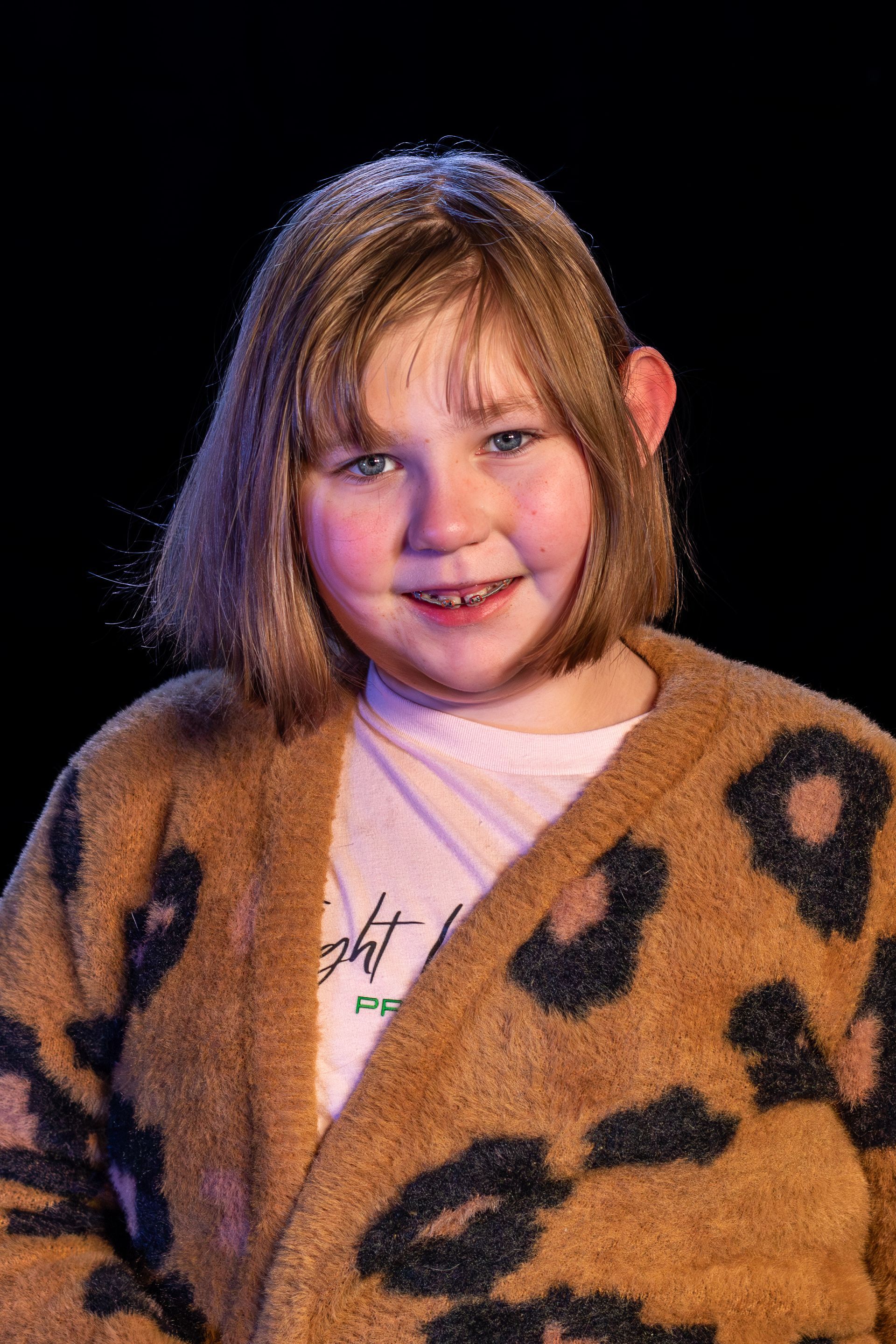 Young person smiles wearing leopard print cardigan.