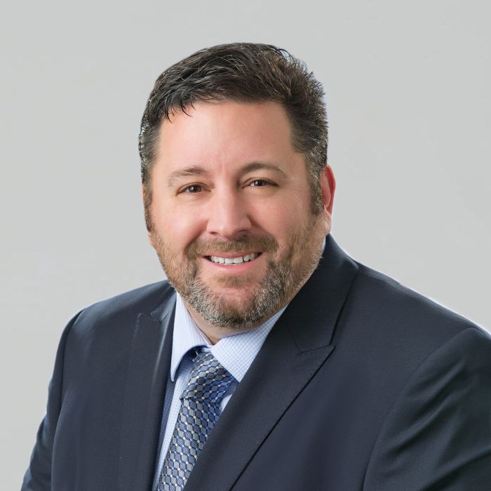 A man in a suit smiles, looking directly at the camera.