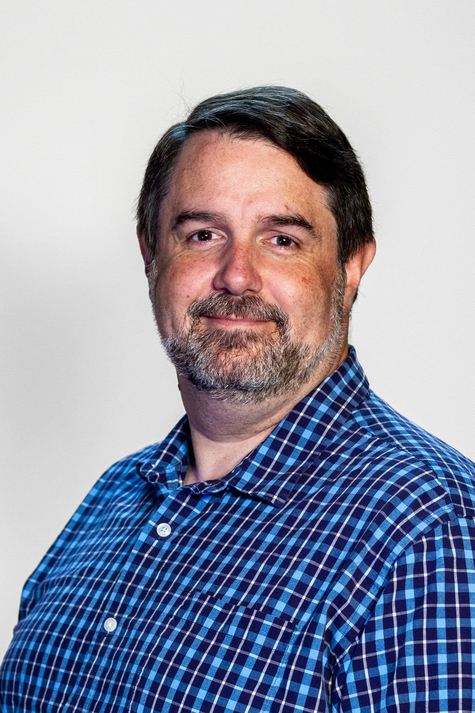 Man with beard in blue plaid shirt, smiling.