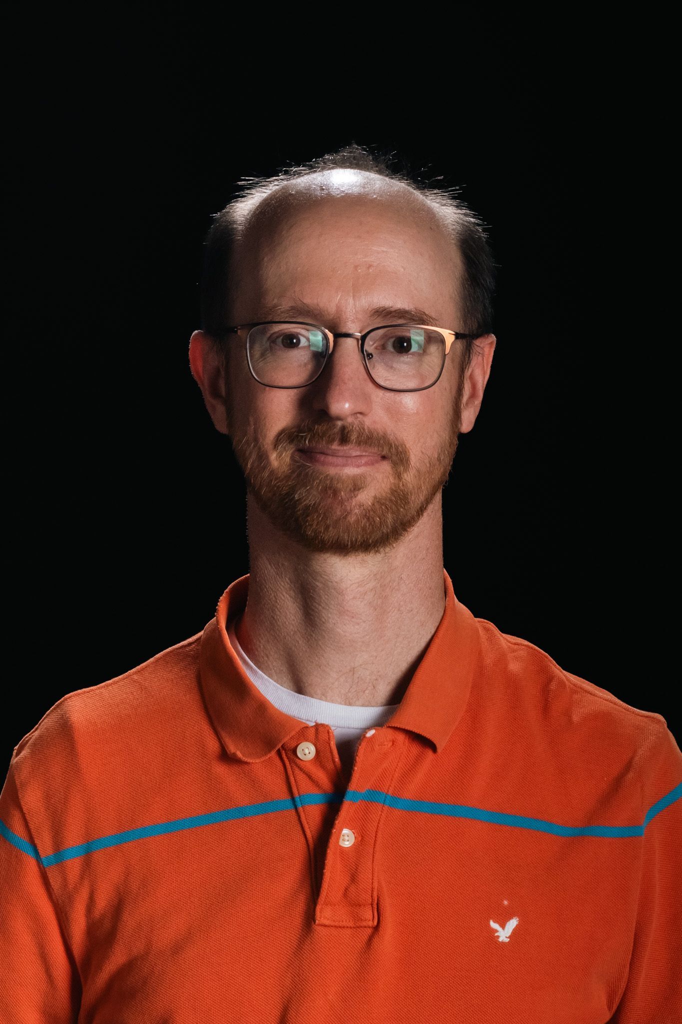 Man wearing glasses and an orange collared shirt against a black background