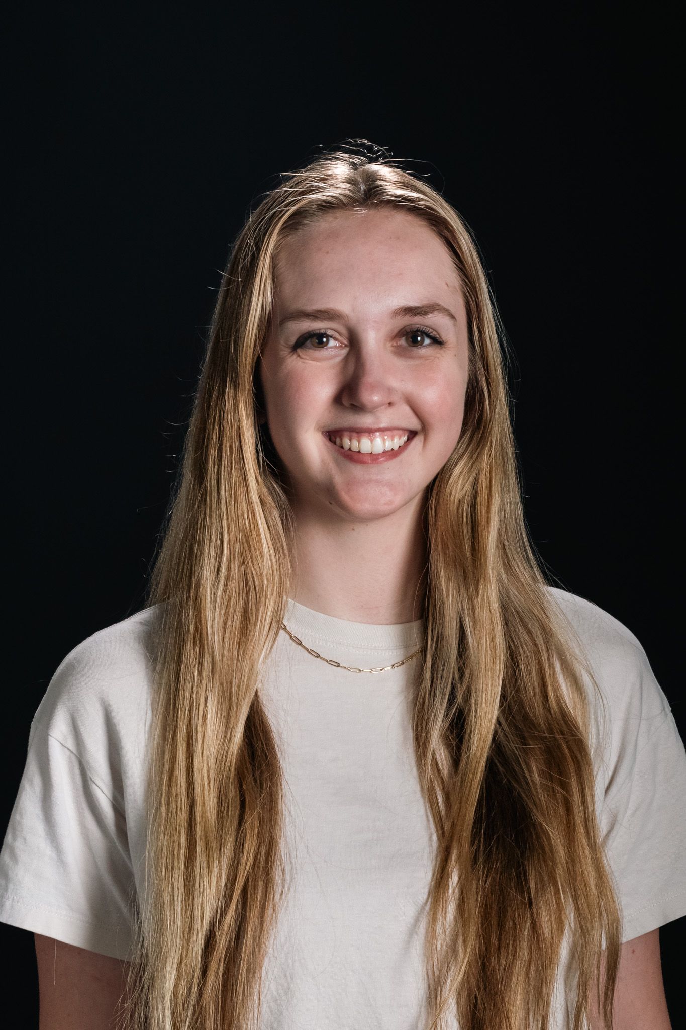 Smiling person with long blonde hair wearing a white shirt against a black background