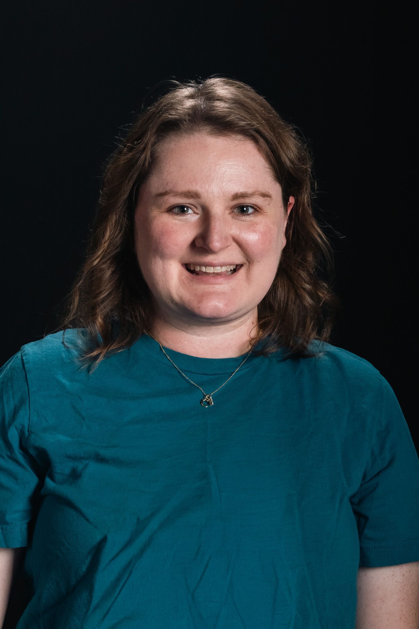 Smiling person in a teal shirt against a dark background