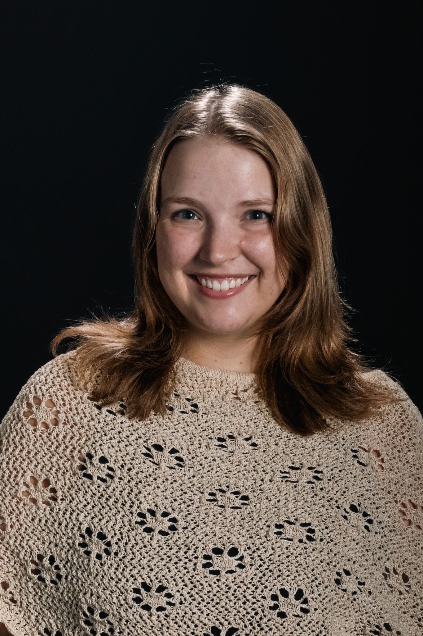 Smiling person in a beige patterned sweater against a dark background