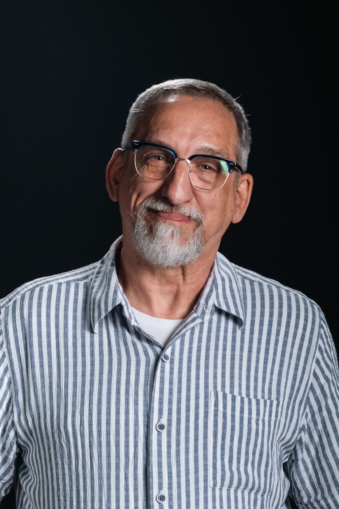 Man smiling gently in a striped shirt against a dark background