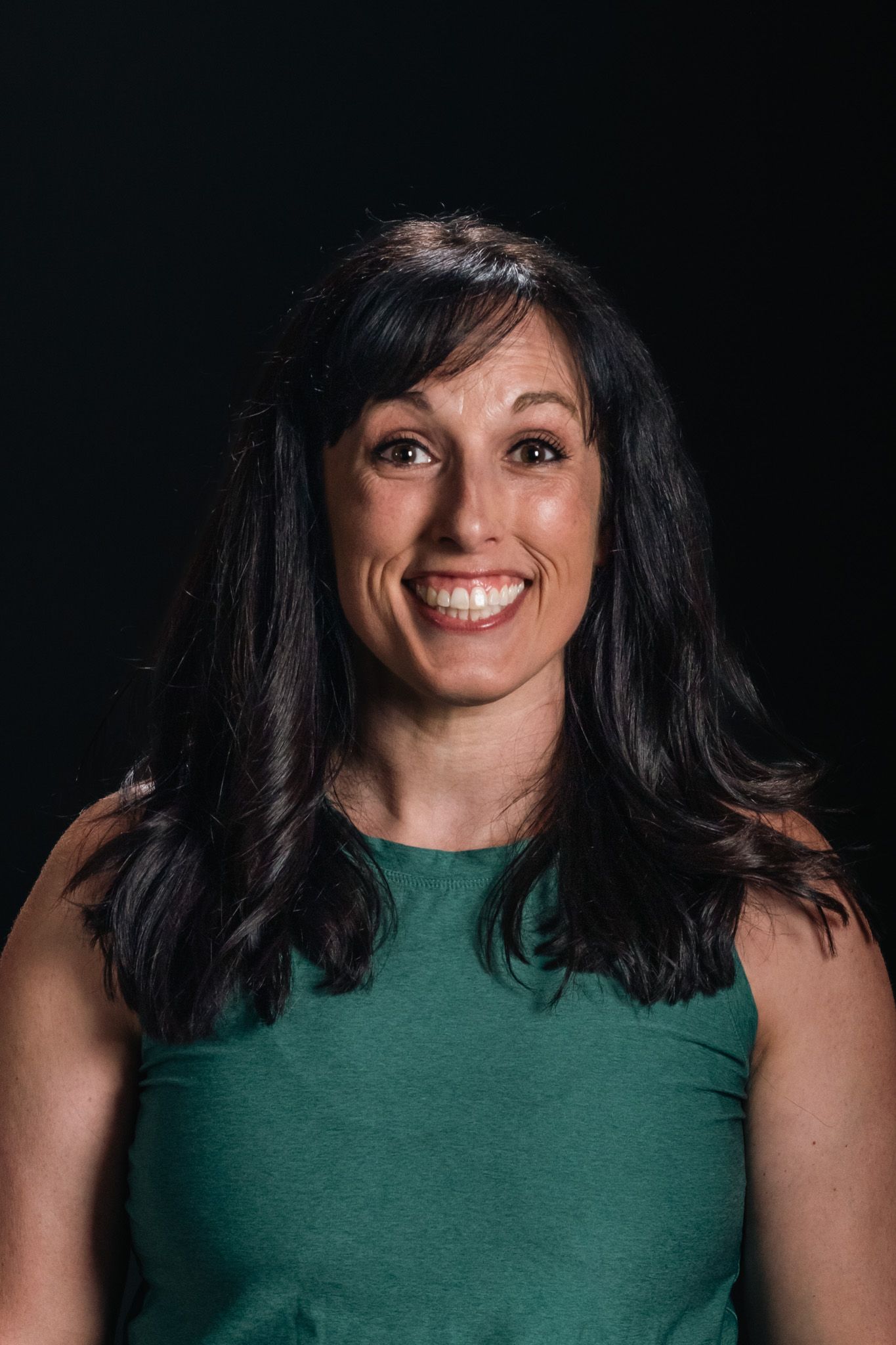 Smiling woman with dark hair wearing a green sleeveless top against a black background