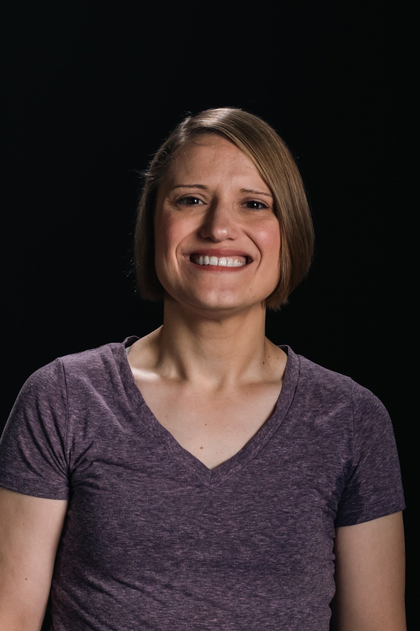 Smiling person in a purple V-neck shirt against a black background