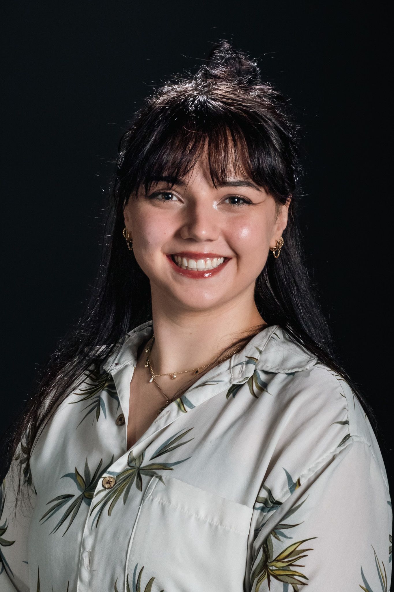 Smiling person in a light floral blouse against a dark background