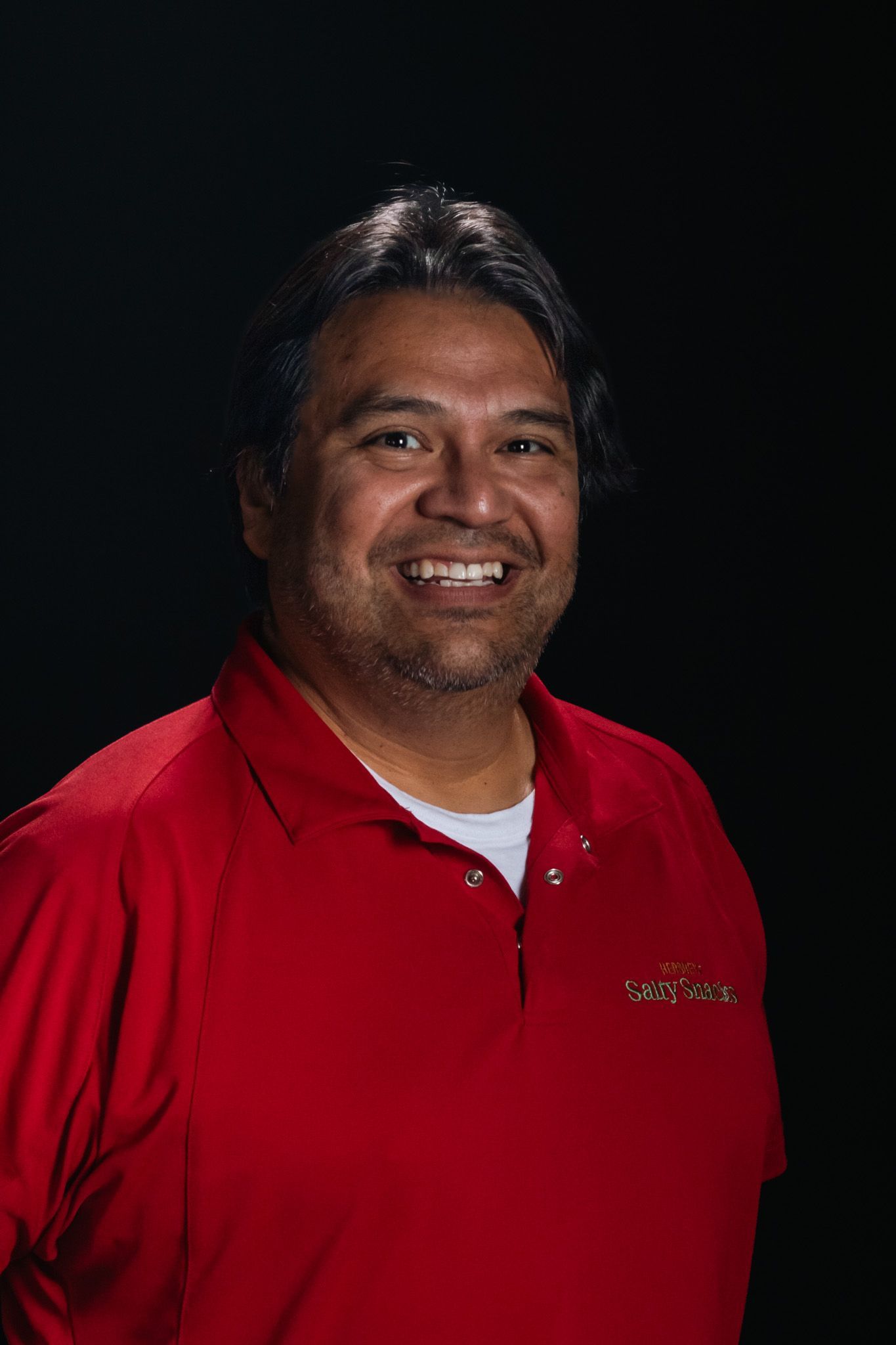 Man smiling in a red polo shirt against a dark background