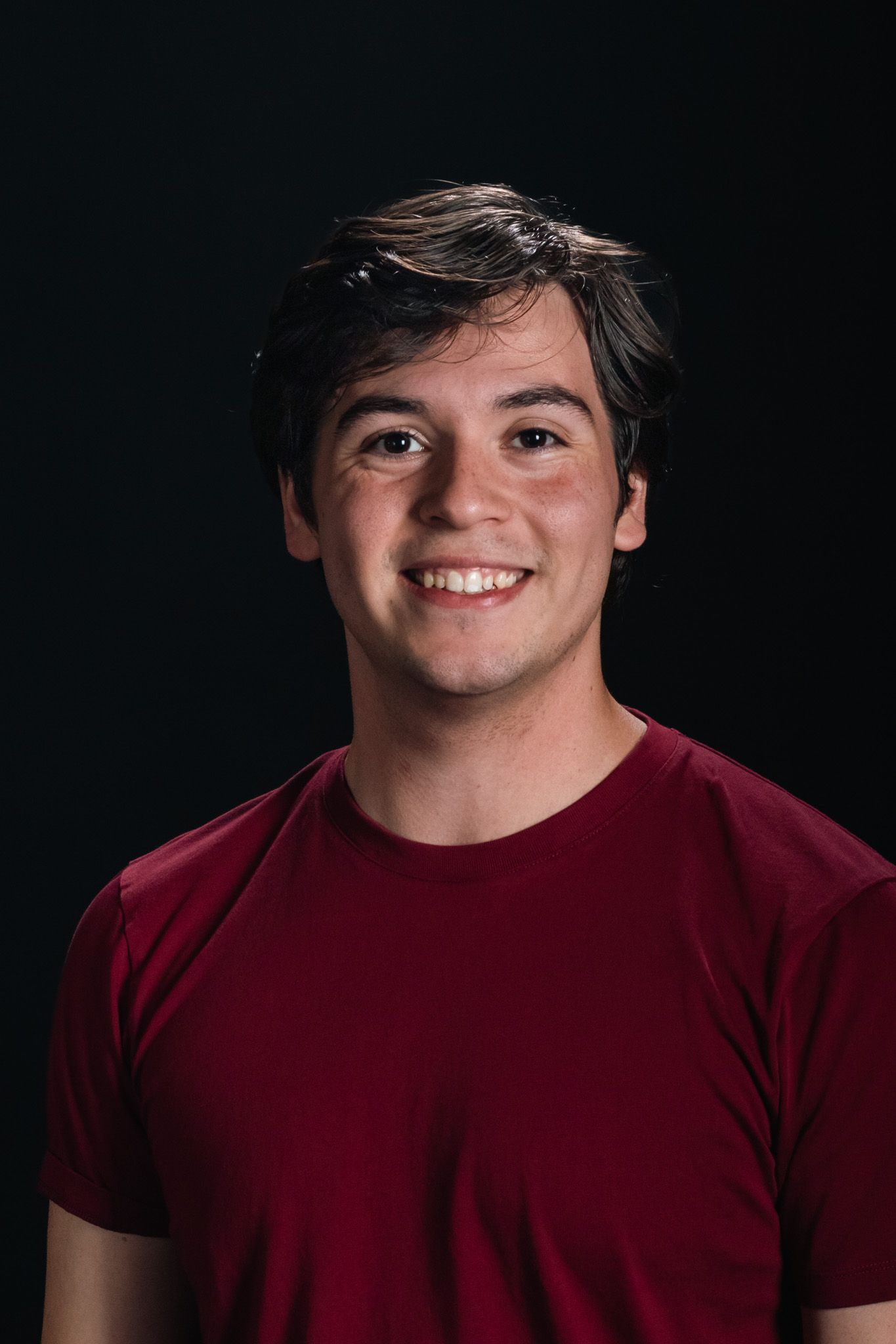 Smiling person in a red shirt against a dark background