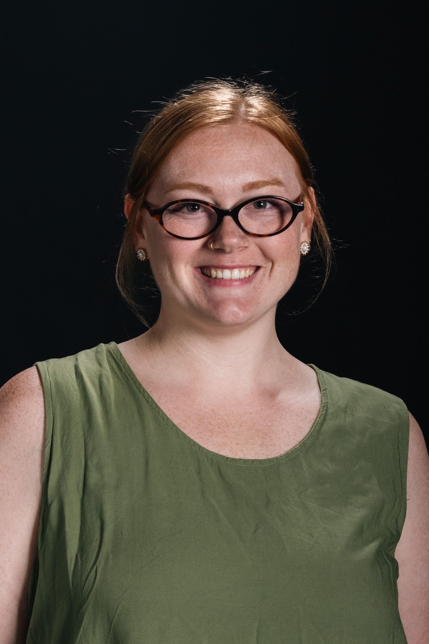 Smiling person with glasses wearing a green sleeveless top against a dark background