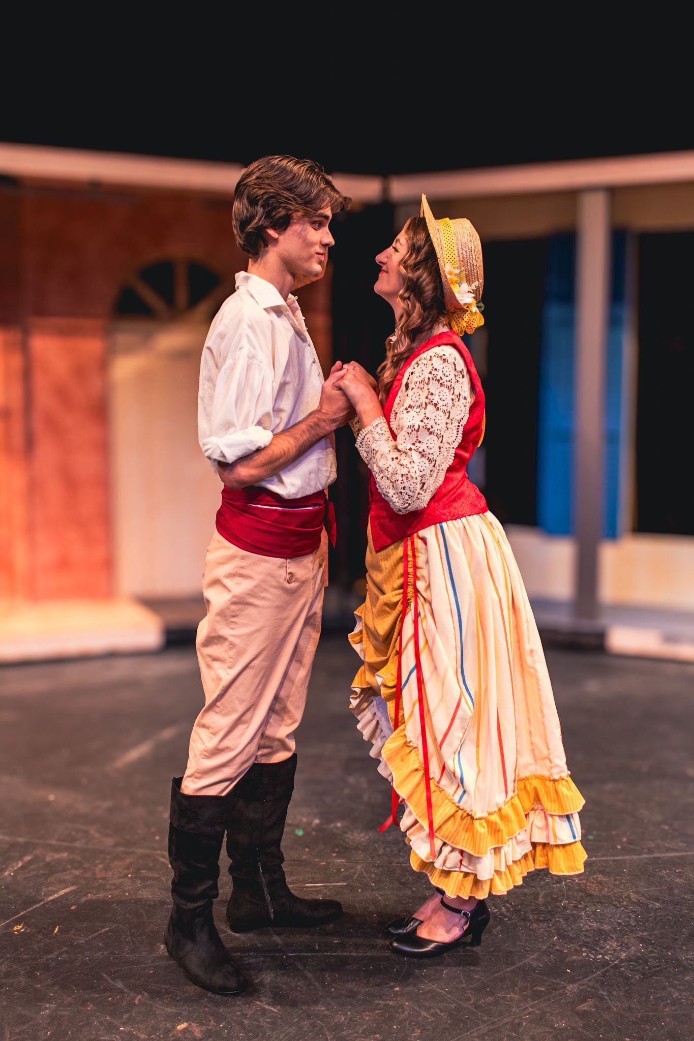 Two performers in period costumes stand face to face on a stage