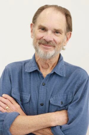 Smiling man in a blue shirt with arms crossed against a plain light background
