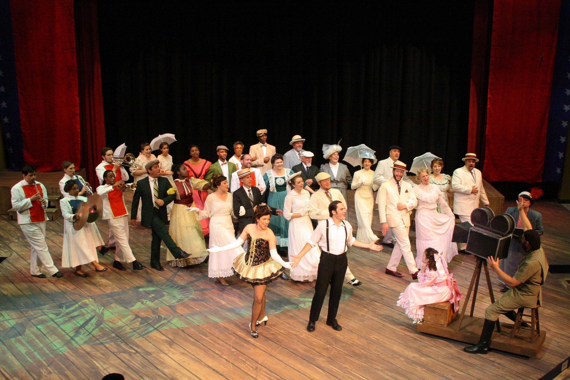 A production with actors in period costumes, centered around a man with suspenders and a woman in a tutu, with a film crew.