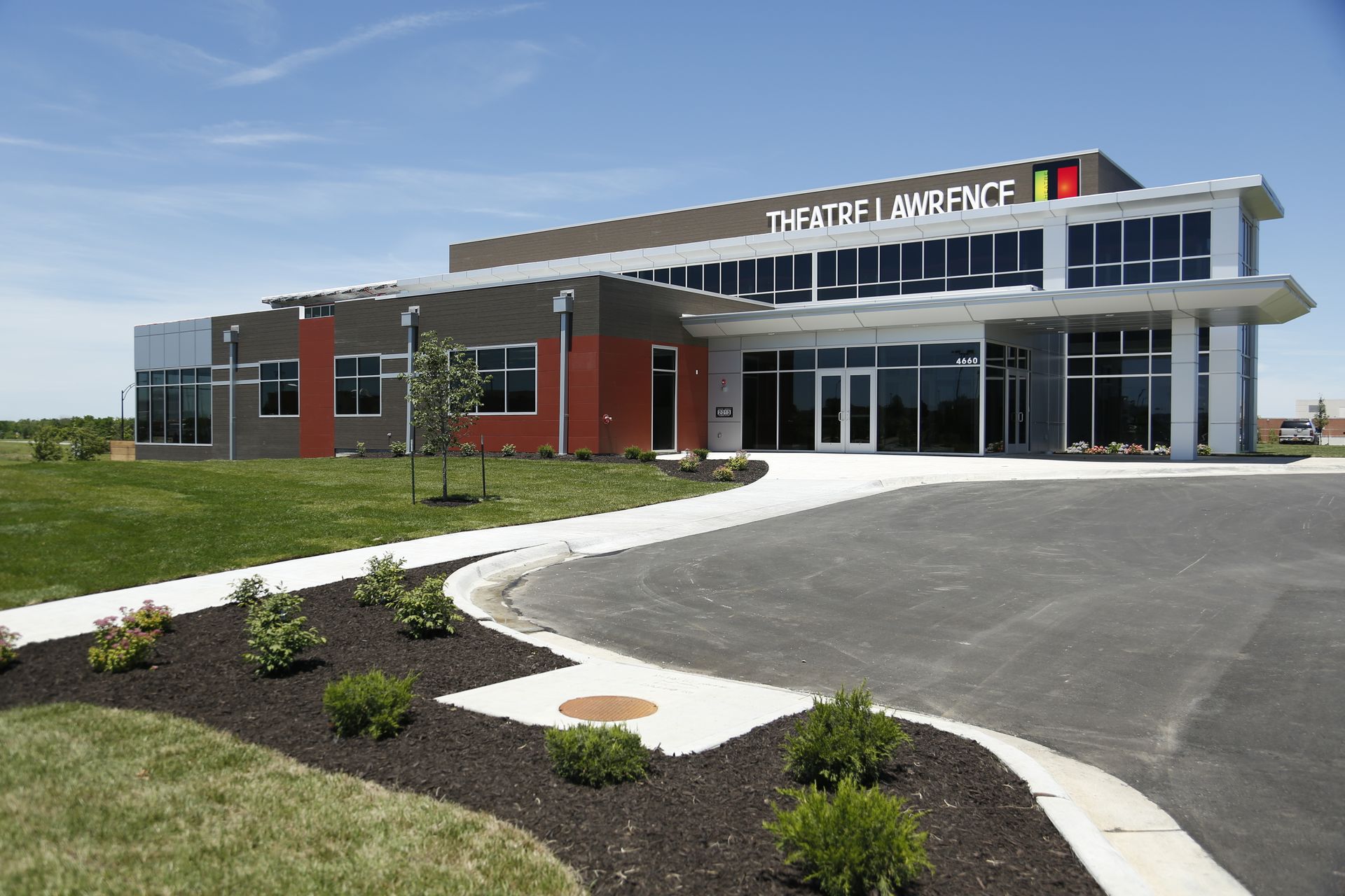 Current facility upon opening in 2013 Modern building with glass facade, red, gray, and brown accents, blue sky, and green lawn.