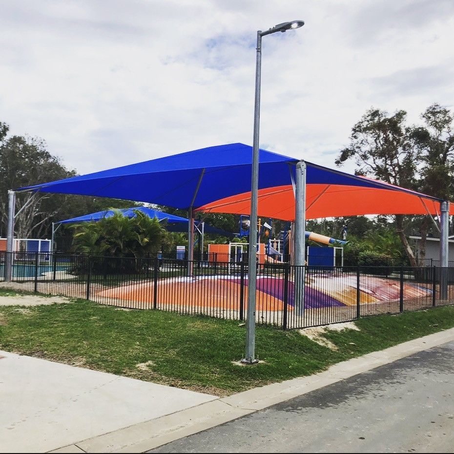 A blue and orange umbrella is covering a playground in a park — SPF Shades and Sails in Tweed Heads West, NSW