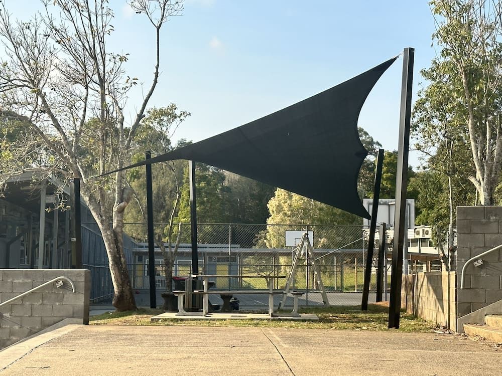 A Large Black Umbrella Is Sitting On Top Of A Concrete Surface In A Park — SPF Shades and Sails in Tweed Heads West, NSW