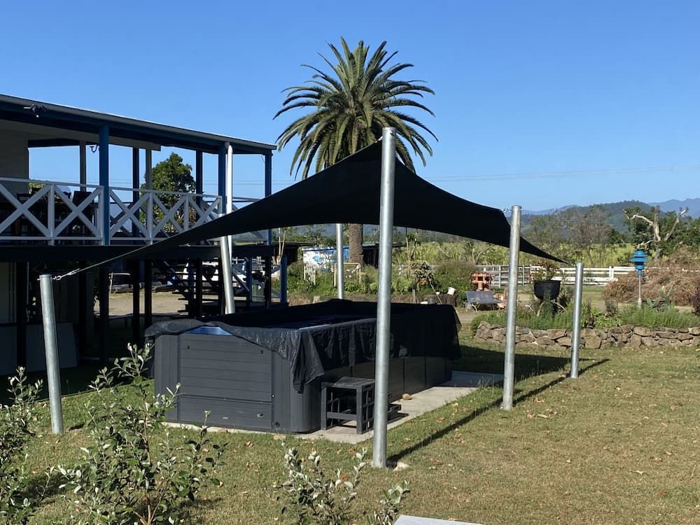 A Black Umbrella Is Covering A Hot Tub In Front Of A House — SPF Shades and Sails in Tweed Heads, NSW