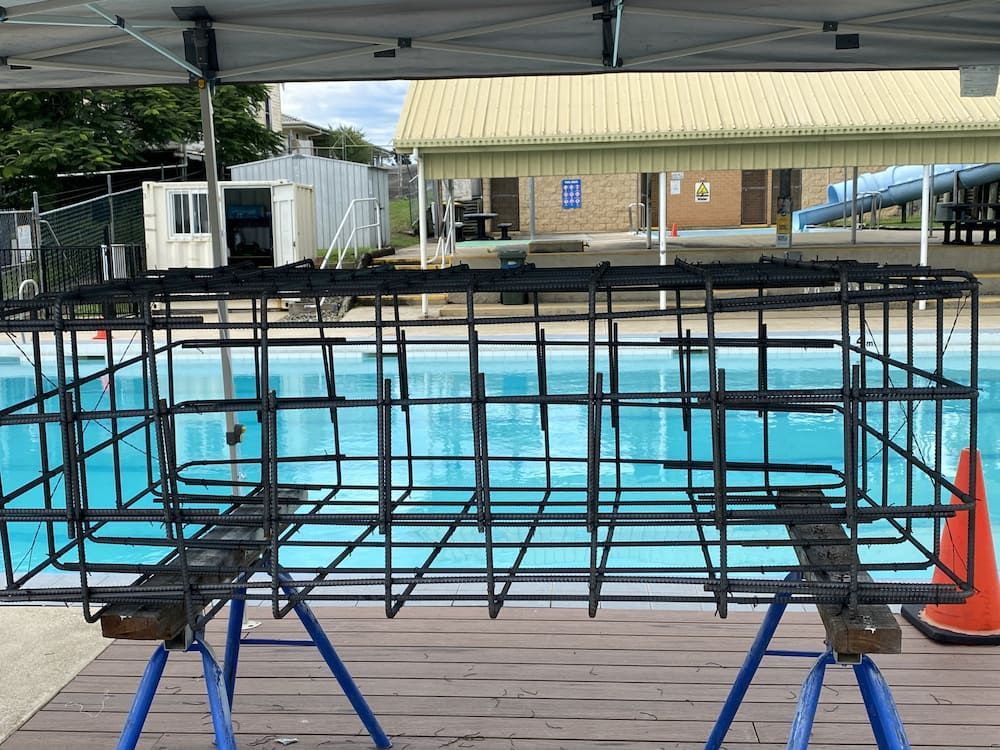 A Metal Cage Is Sitting On A Wooden Deck Next To A Swimming Pool — SPF Shades and Sails in Tweed Heads West, NSW
