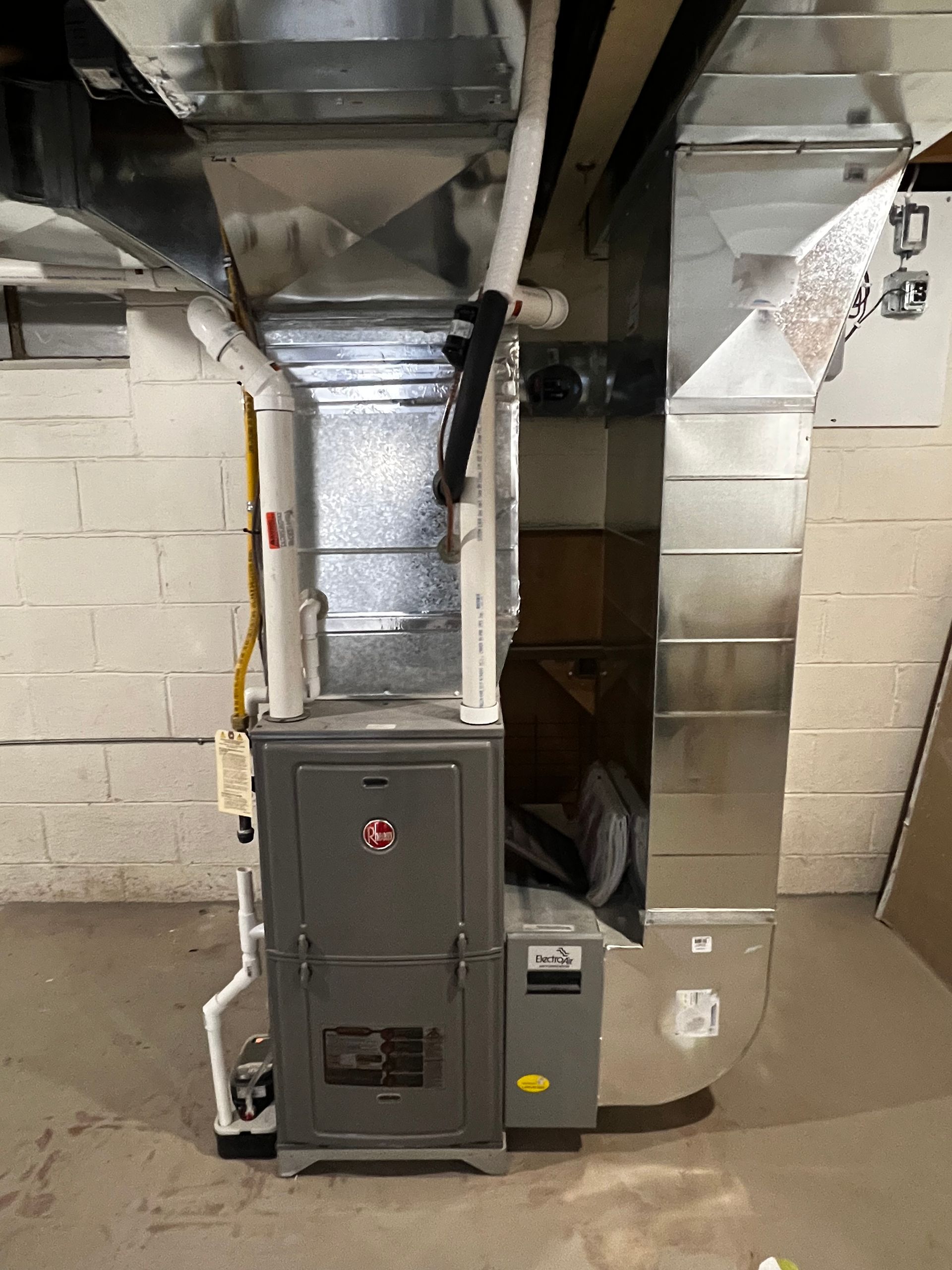 A furnace is sitting in a basement next to a brick wall.