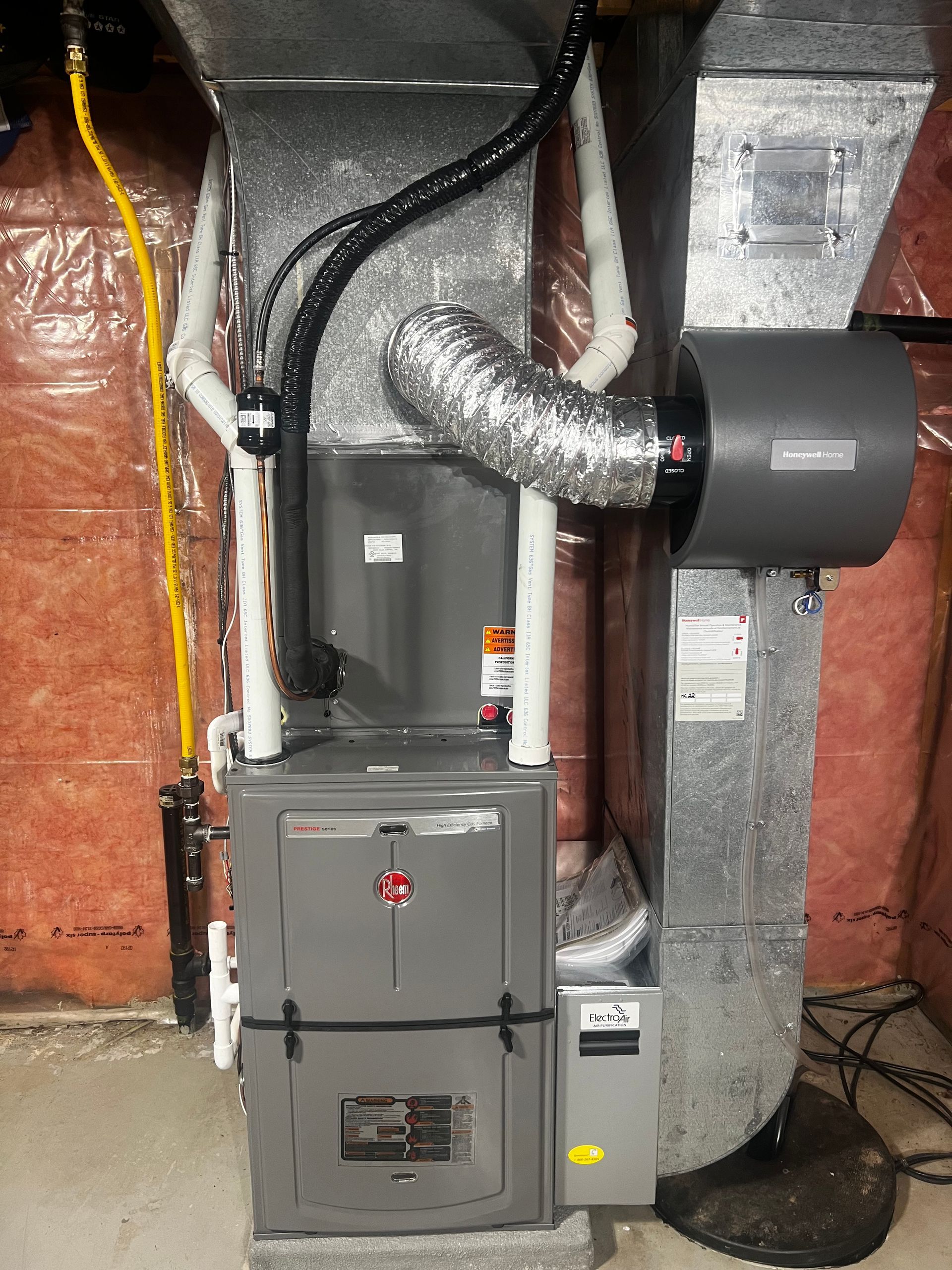 A furnace is sitting in a basement next to a fan.