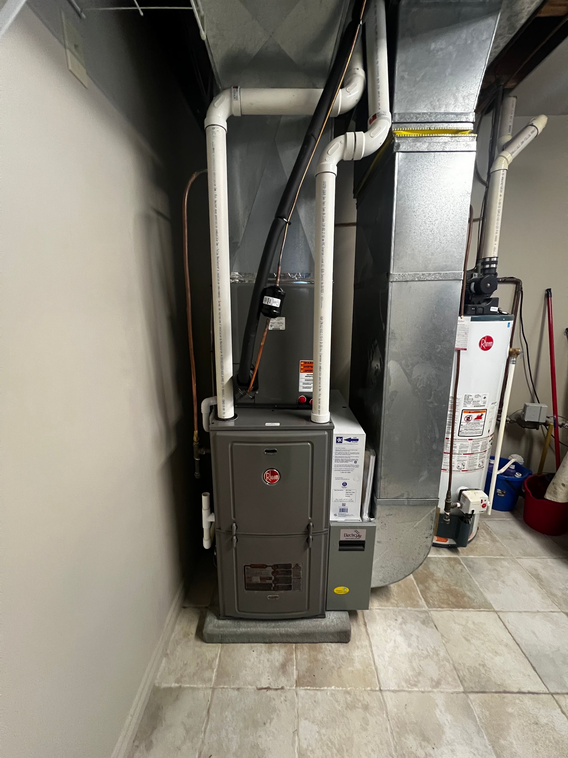A gas heater is sitting in a basement next to a water heater.