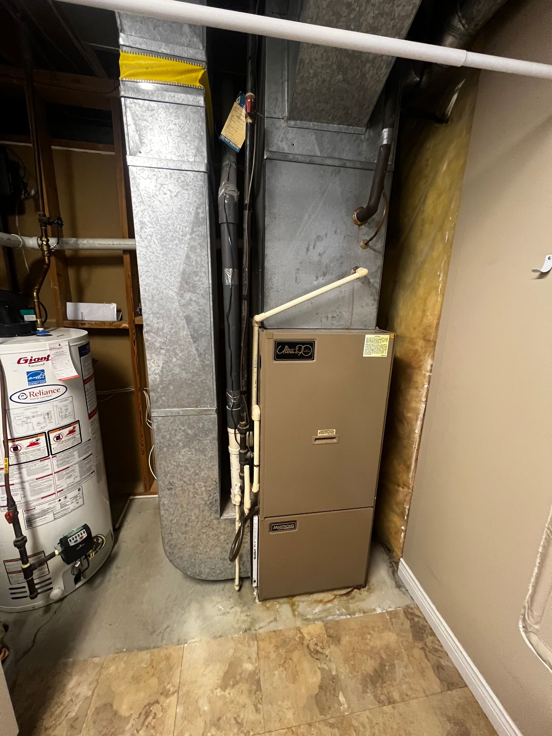 An air conditioner is sitting in a basement next to a water heater.