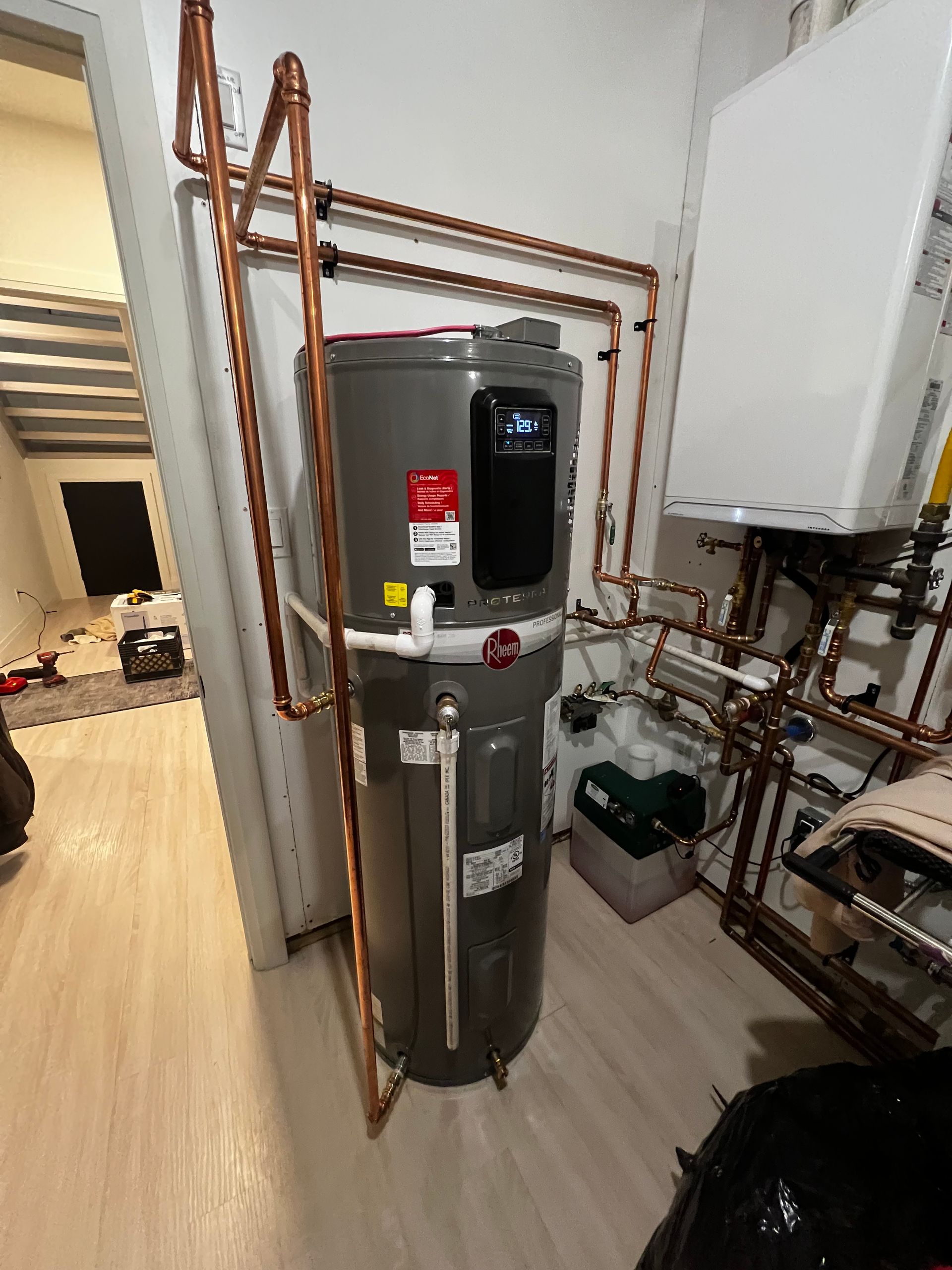A water heater is sitting in a room with copper pipes.