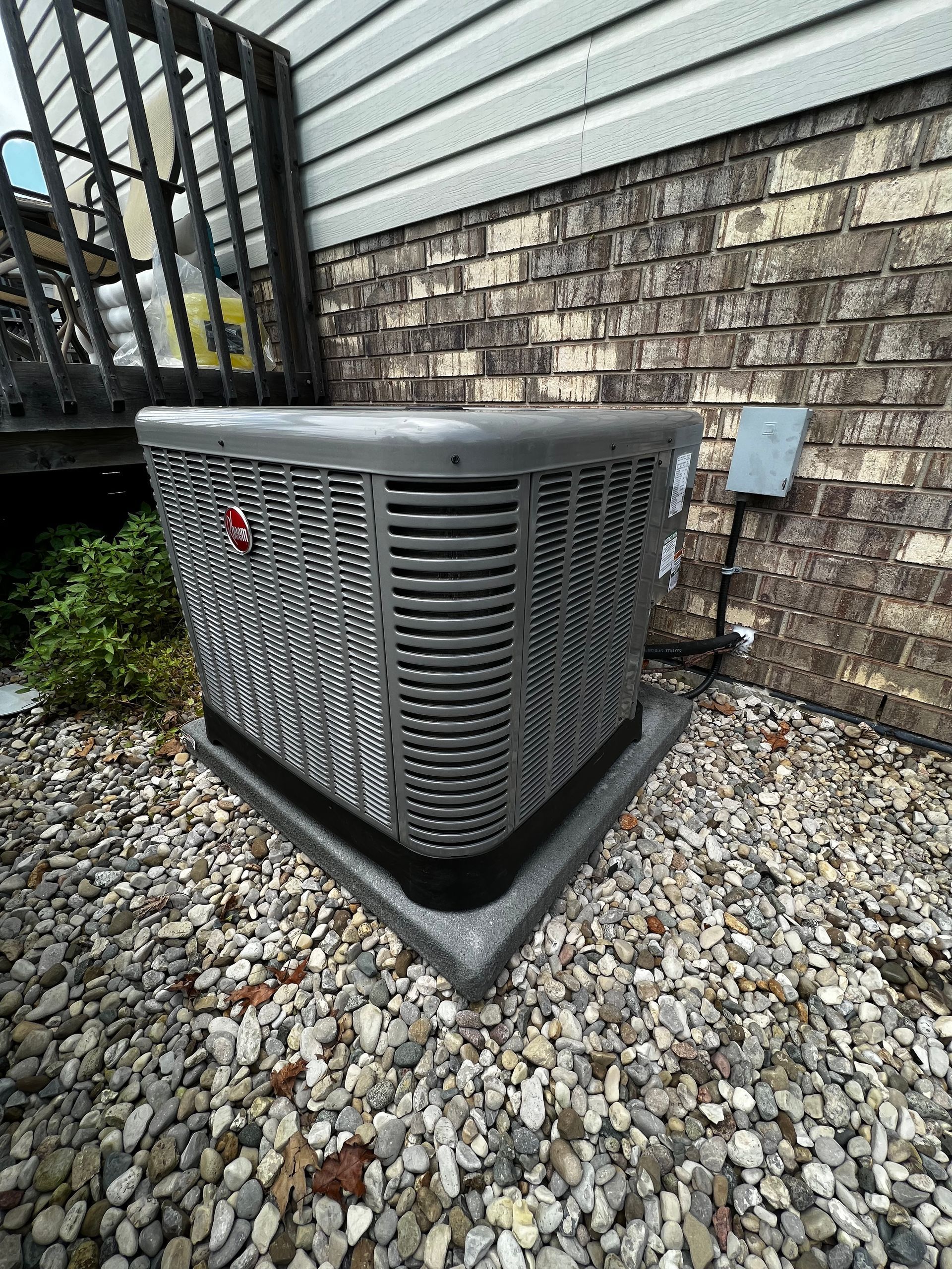 A large air conditioner is sitting on top of a pile of gravel in front of a brick building.