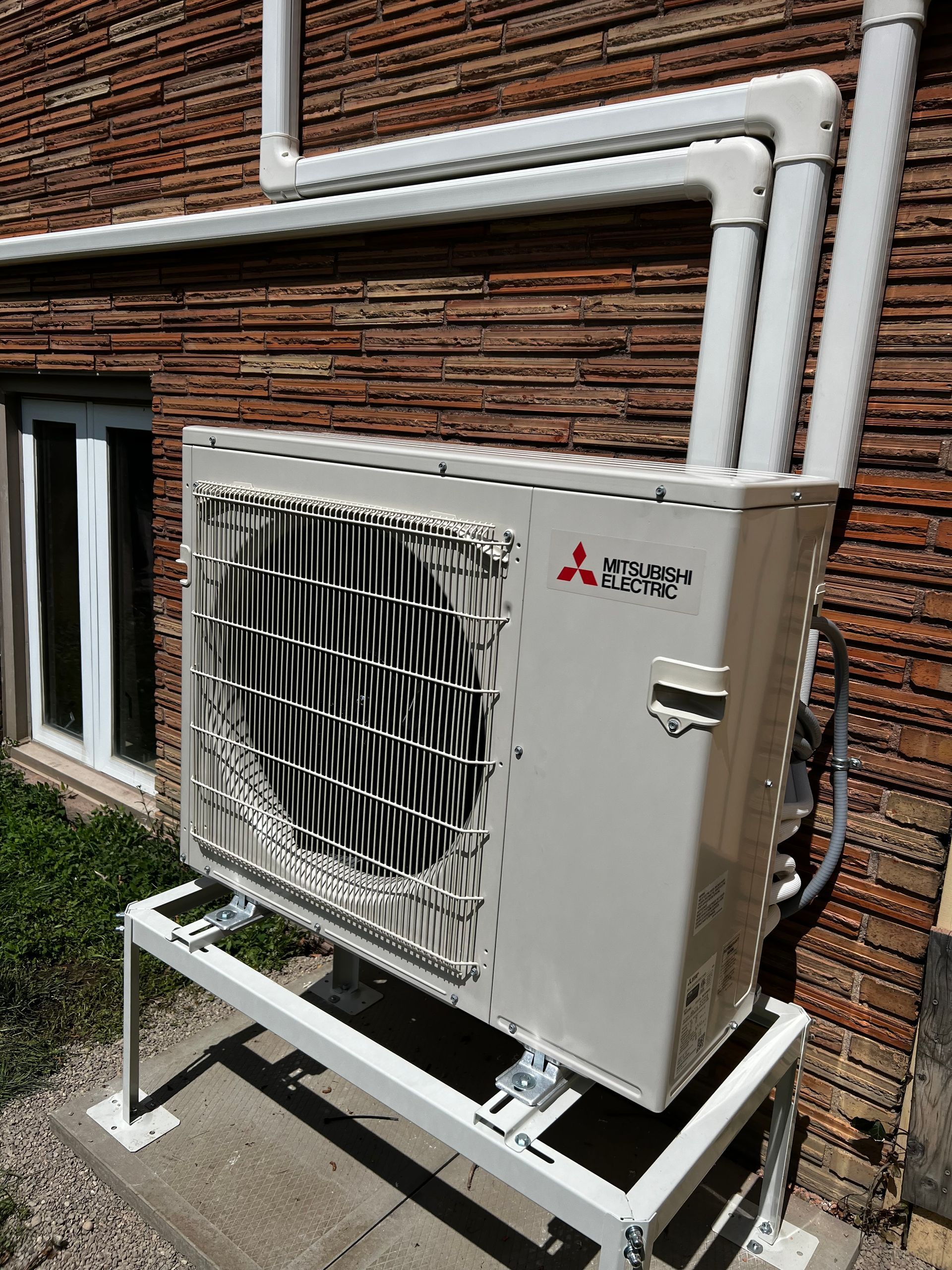 A mitsubishi air conditioner is sitting outside of a brick building.