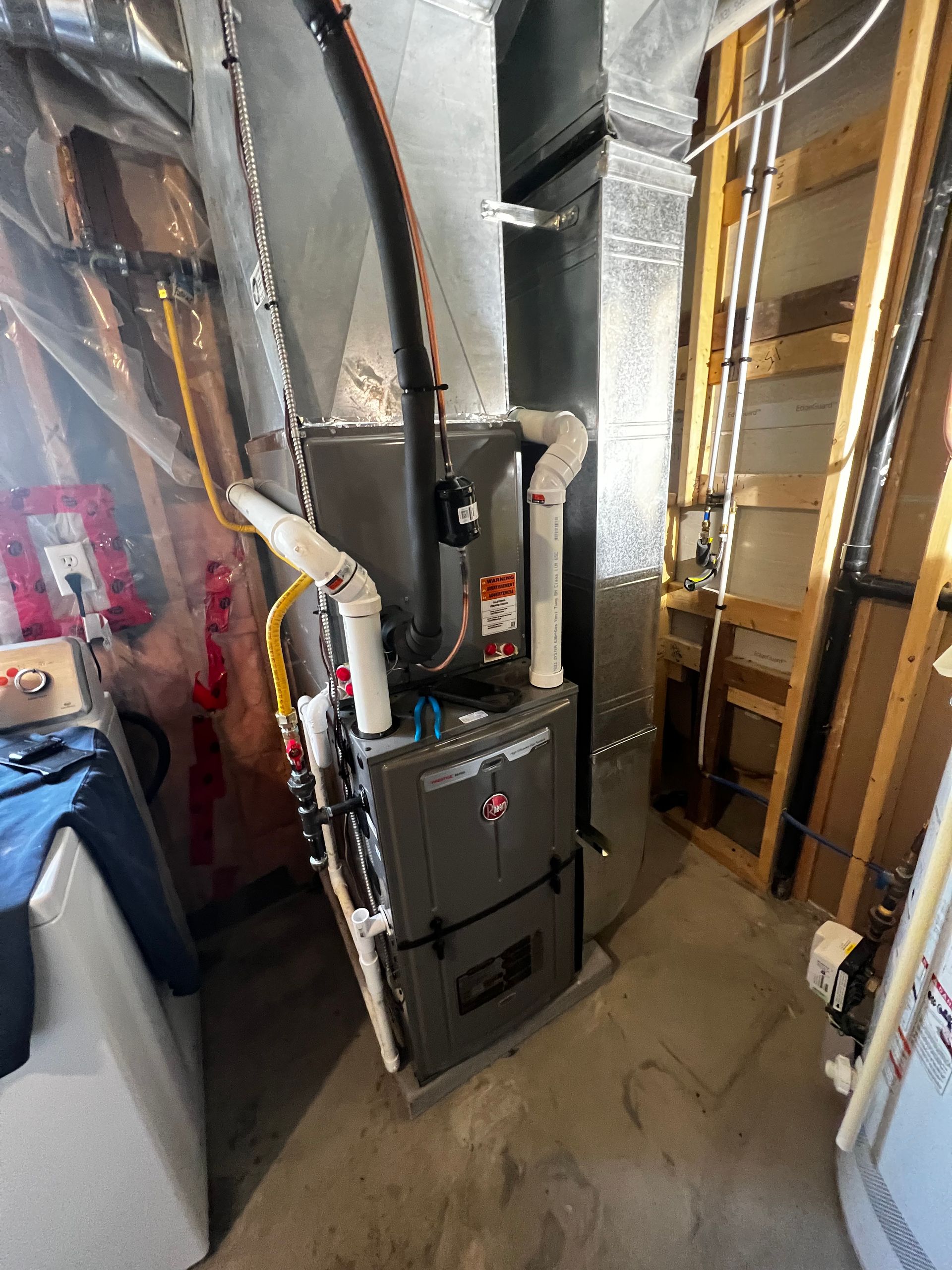 A furnace is sitting in a basement next to a washer and dryer.