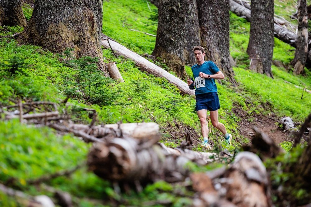 A man is running on a trail in the woods.