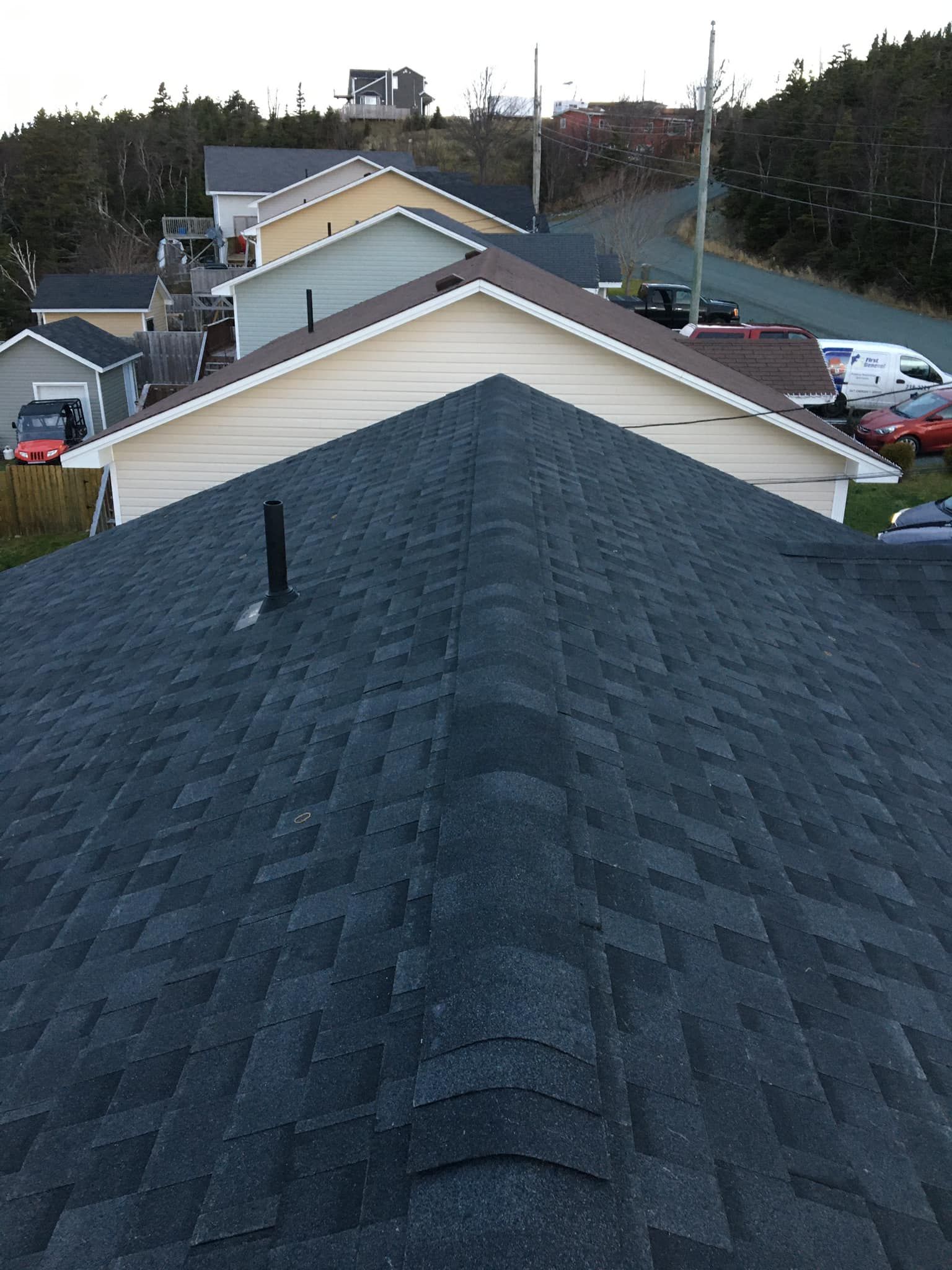 View from a dark shingled roof towards a residential area with houses and vehicles.