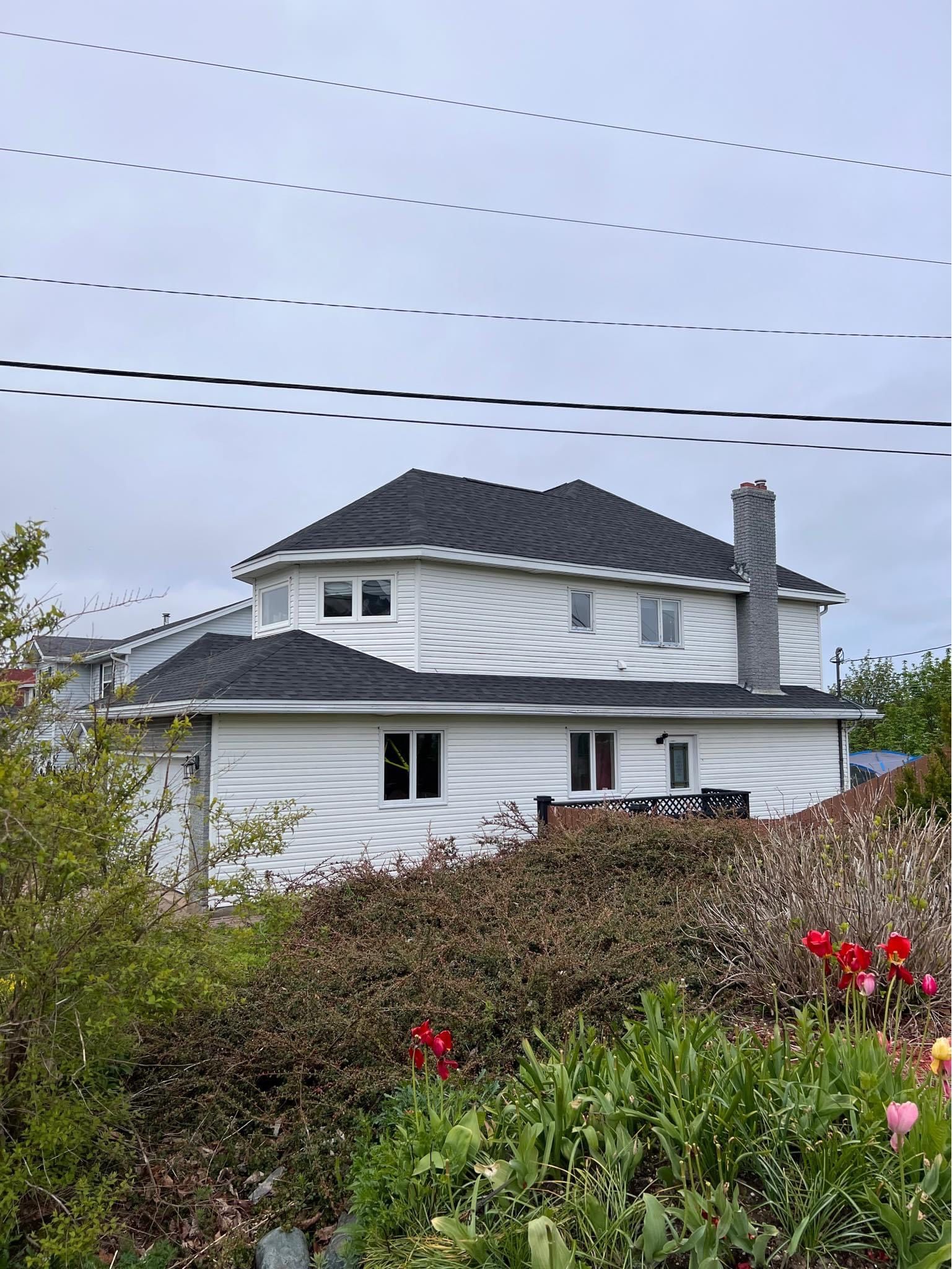 White two-story house with dark roof and brick chimney. Overcast sky.