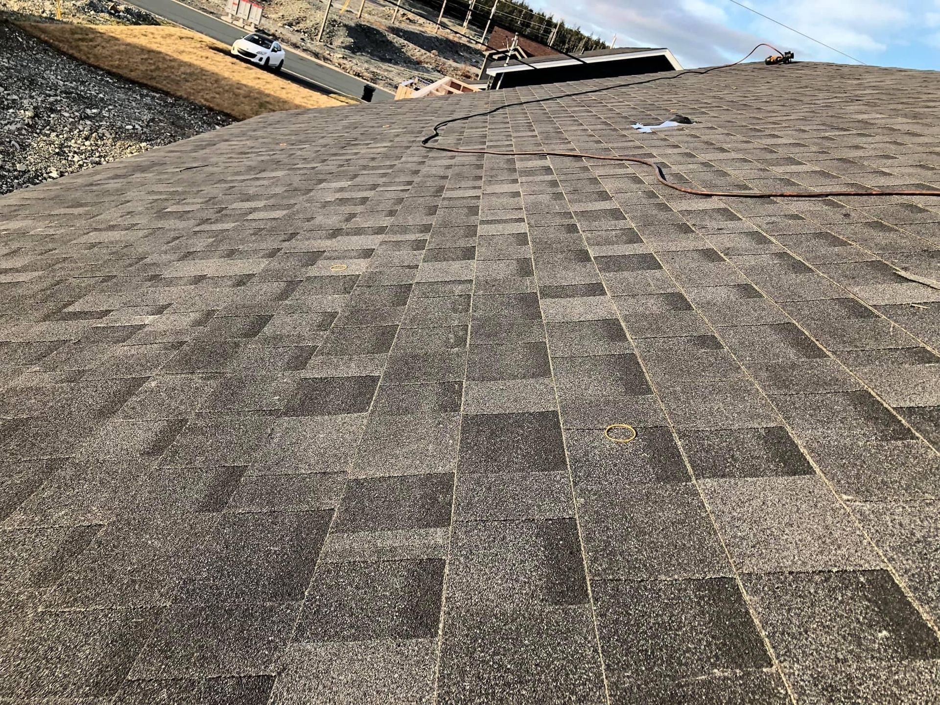 Close-up view of a shingled roof with dark brown and gray asphalt shingles, showing some weathering and damage.