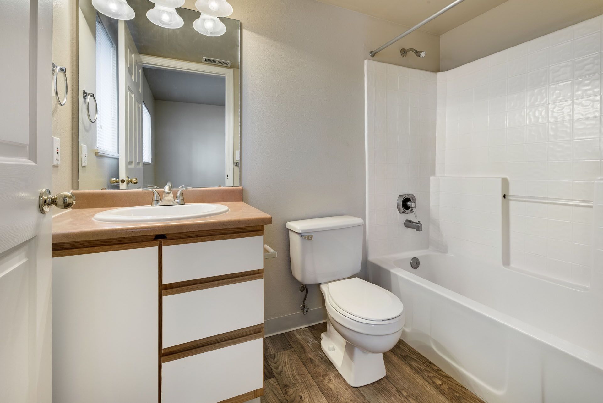 Small bathroom with vanity, toilet, and white bathtub on wood-look floor.