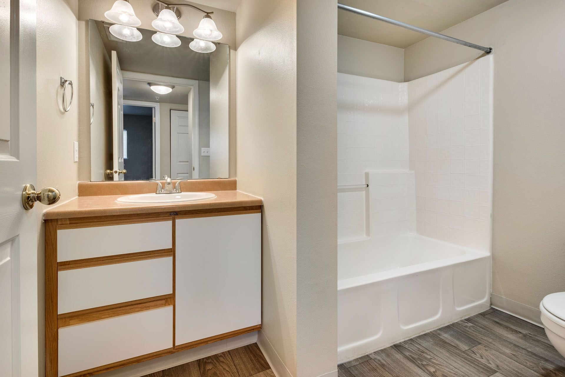 Bathroom with wood vanity, large mirror, and white tiled shower/tub alcove.