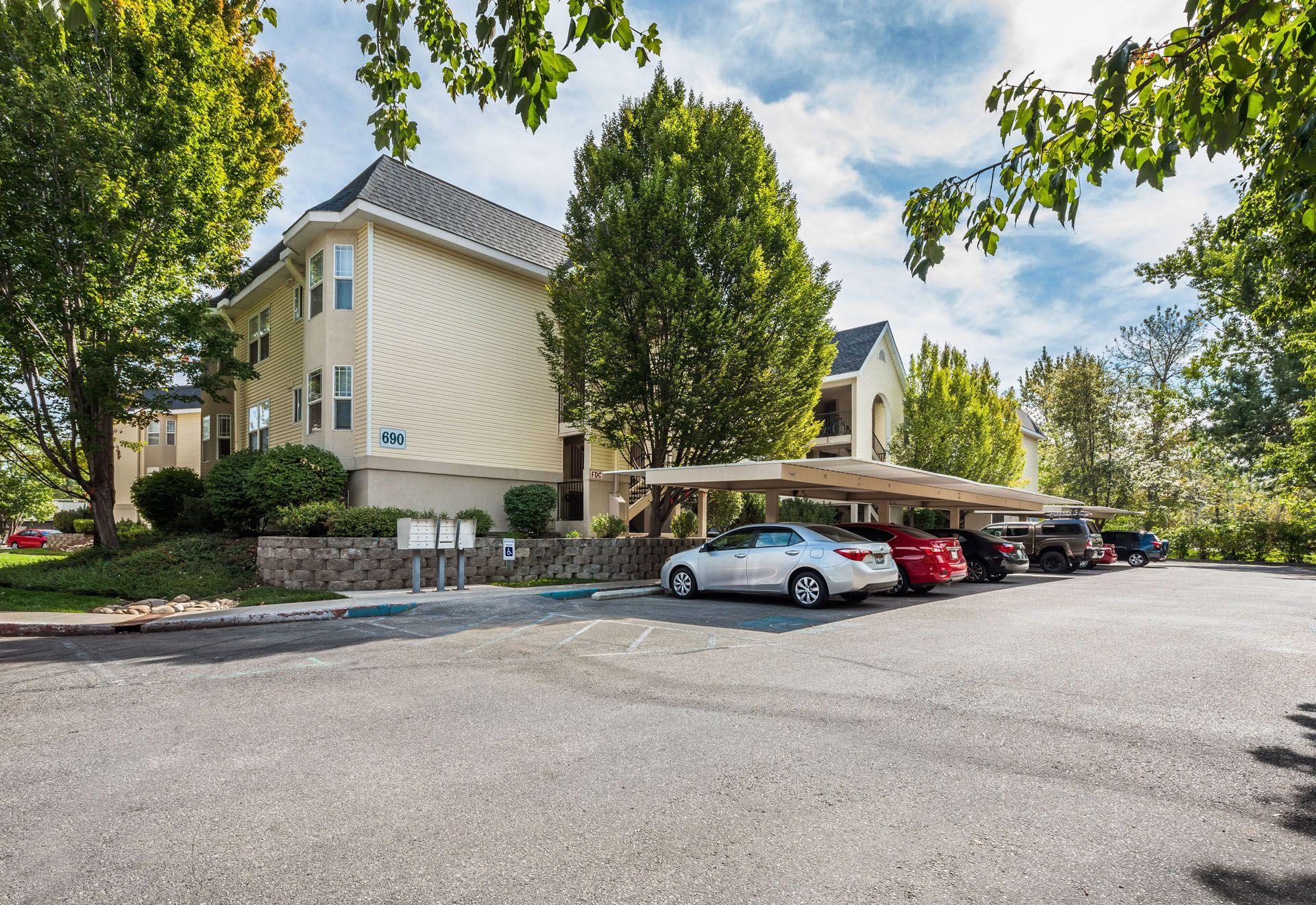 Apartment complex parking lot with parked cars and trees on a sunny day