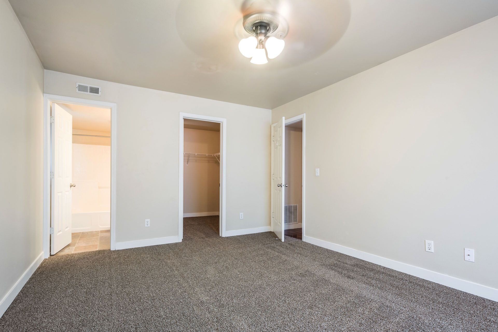 Empty beige bedroom with carpeted floor, ceiling light, and two open doorways.