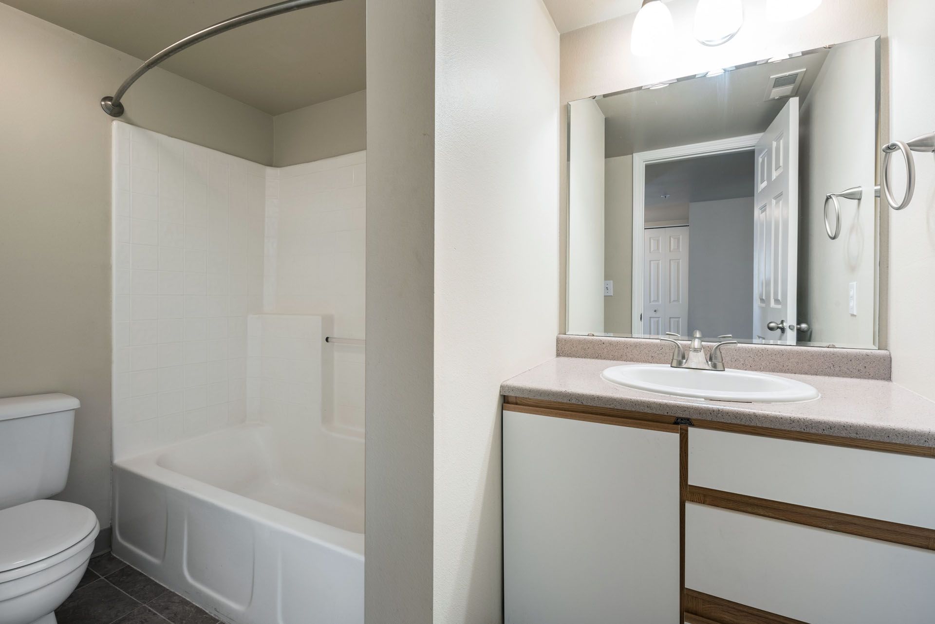 Small bathroom with white tub, toilet, and vanity with mirror and light fixture
