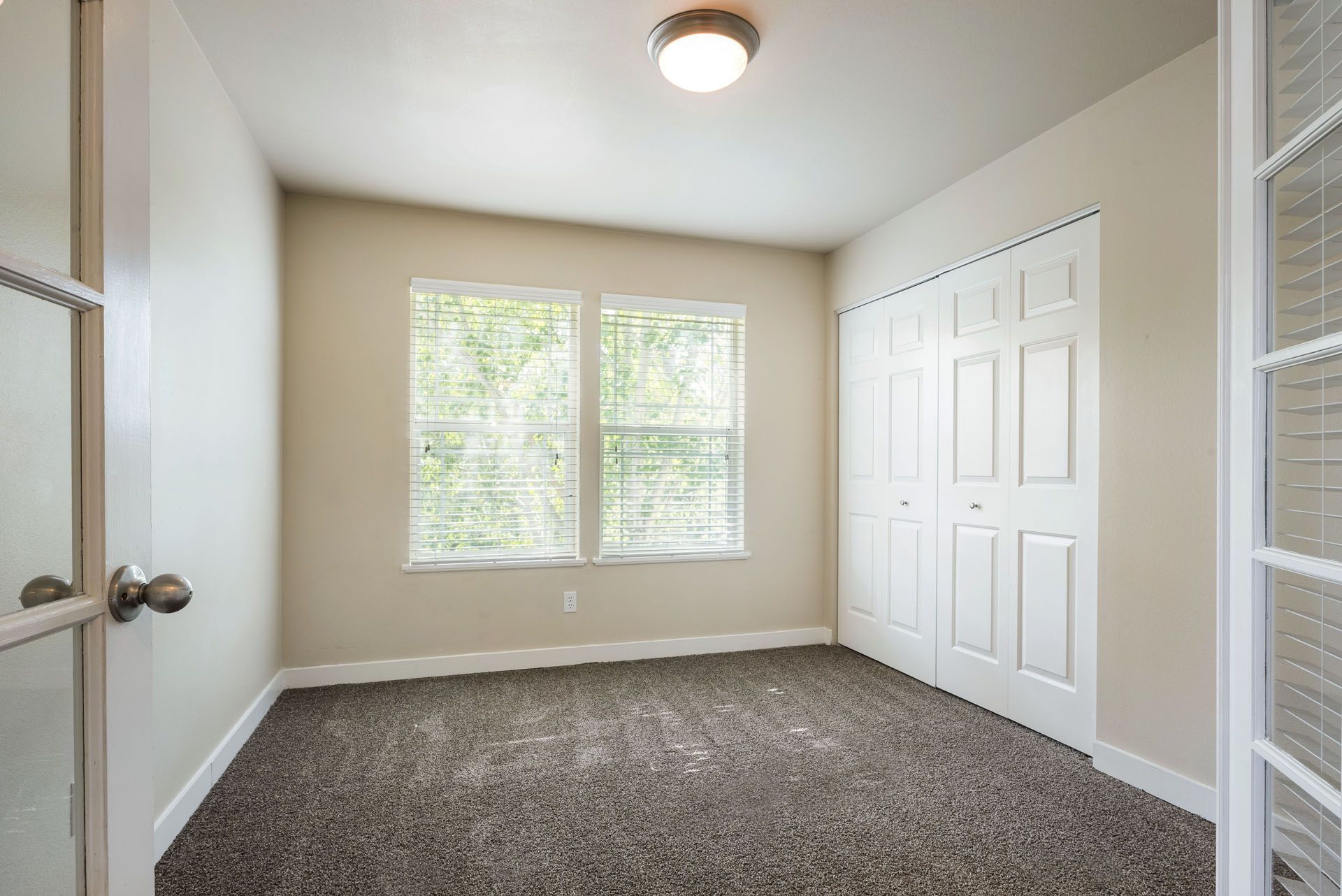 Empty beige bedroom with carpet, window, closet doors, and ceiling light