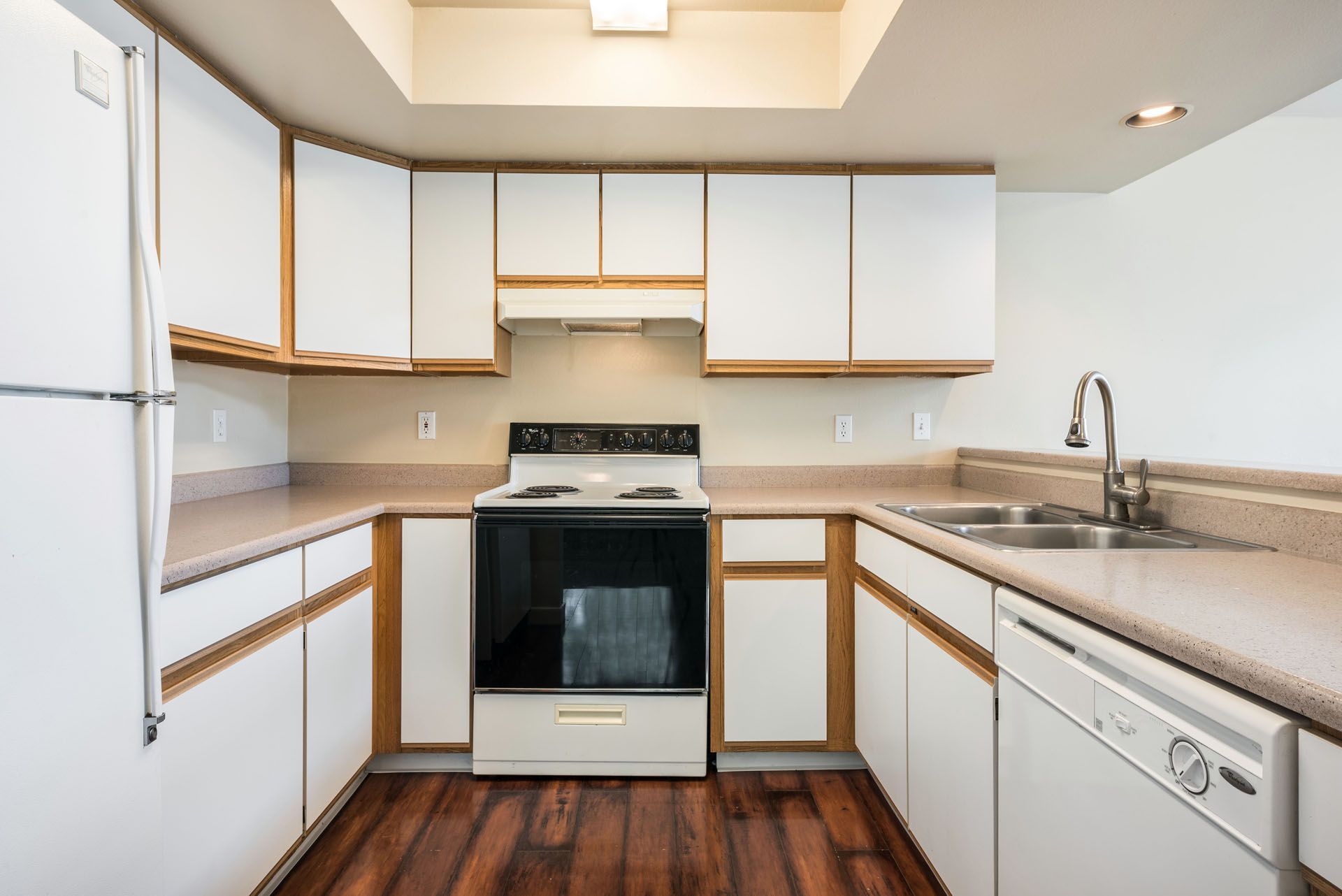 Bright white kitchen with wood trim, stove, sink, dishwasher, and dark wood floor