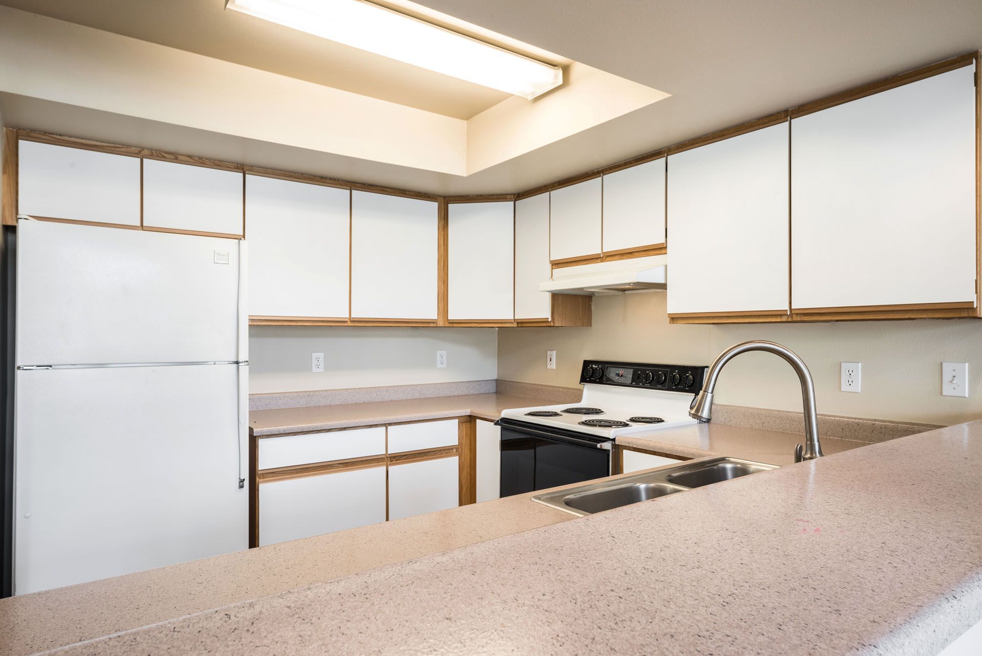 Bright kitchen with white cabinets, stove, sink, refrigerator, and beige countertops