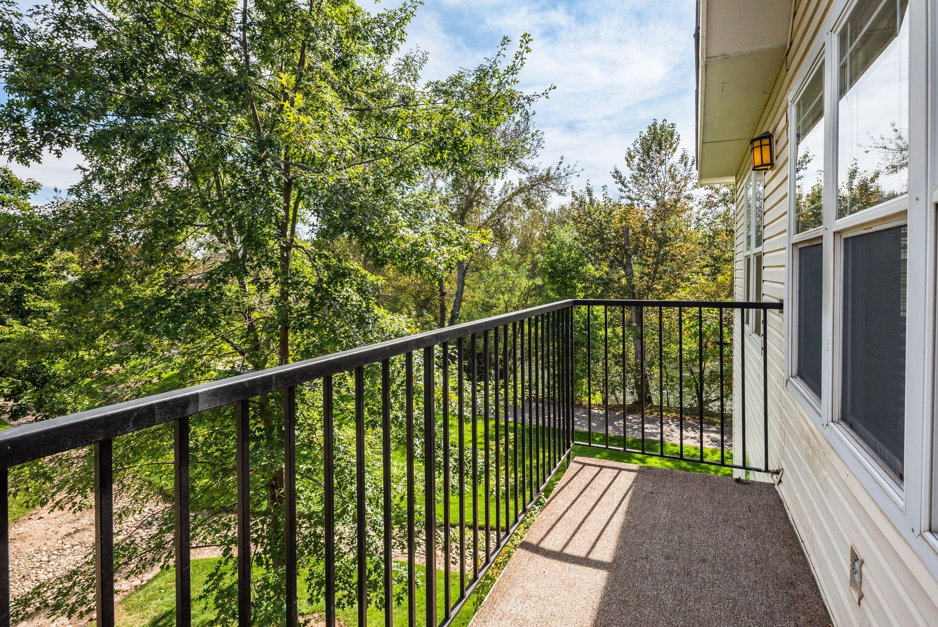Apartment balcony with black metal railing, gravel floor, and green trees below and beside it.
