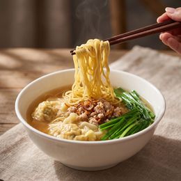 A bowl of noodle soup with chopsticks lifting noodles and greens on the side