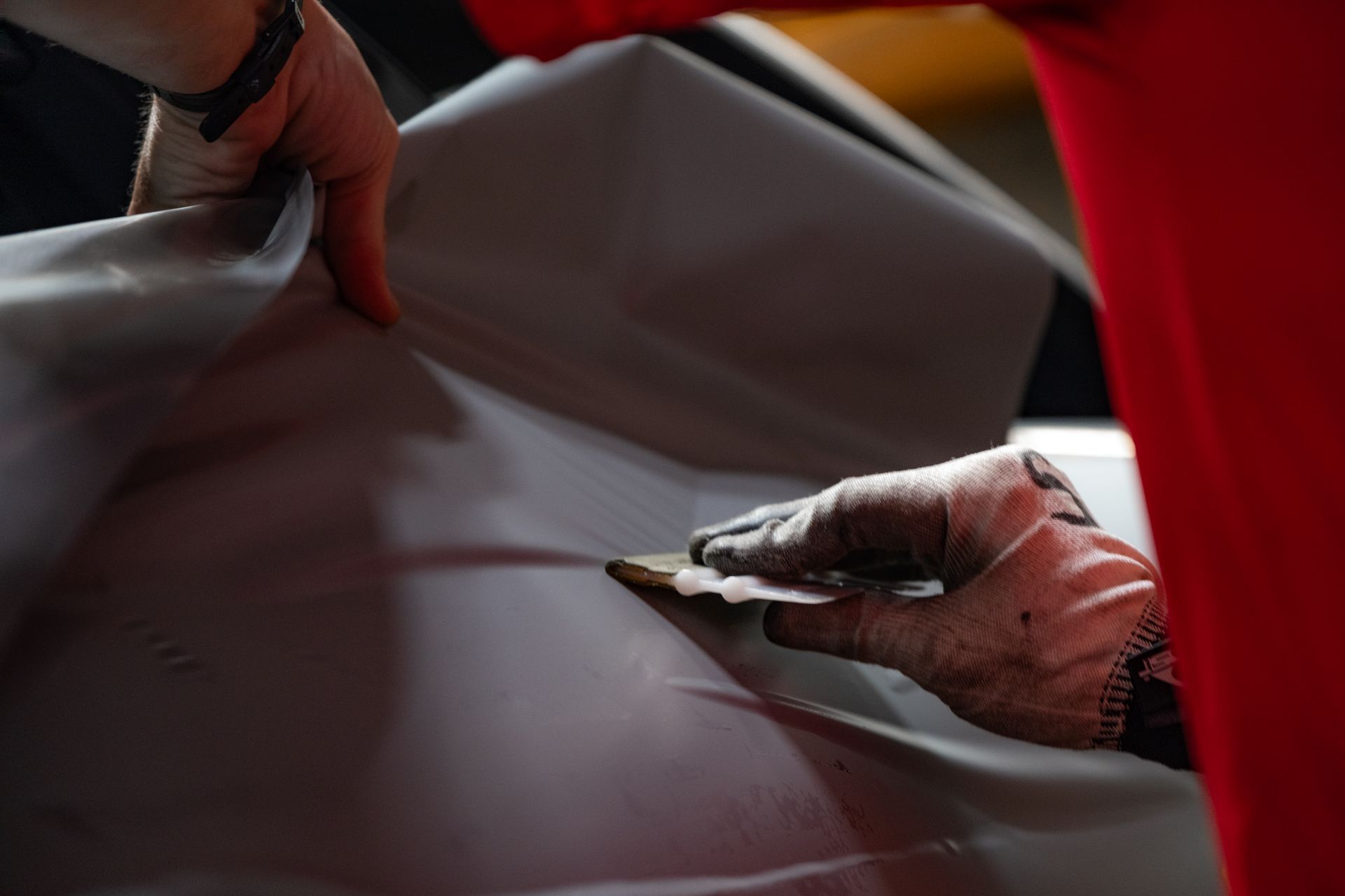 Gloved hands smoothing dark brown leather with a tool during upholstery work
