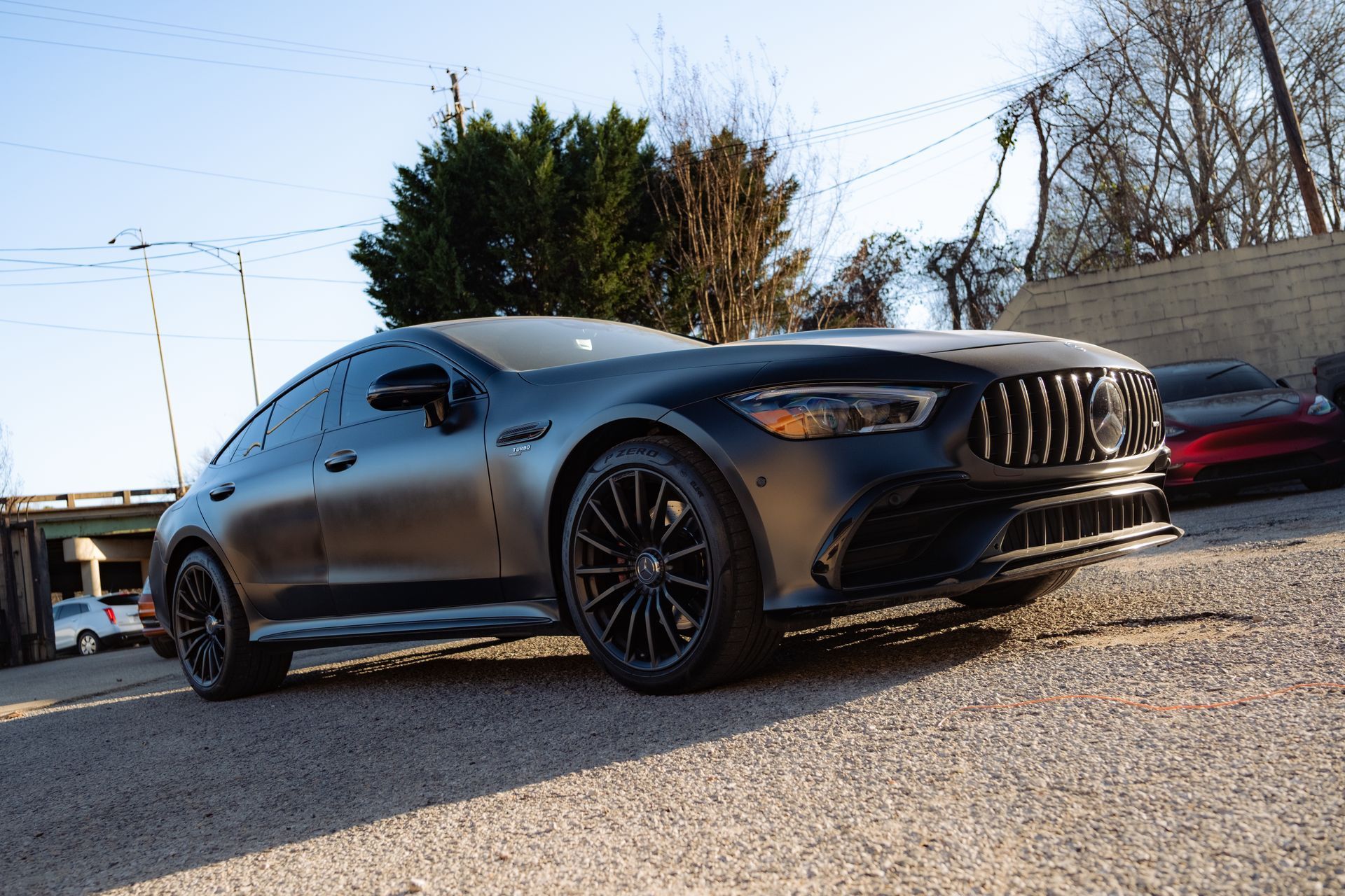 Black sports sedan parked on gravel beside a red car under a clear sky